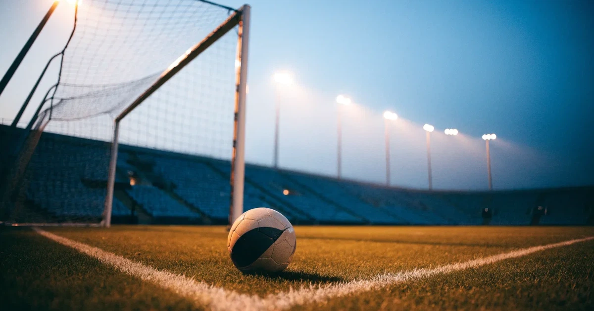 Ein Fußball liegt im Strafraum direkt vor dem Tor mit Netz, im Hintergrund leere Ränge bei Dämmerung.
